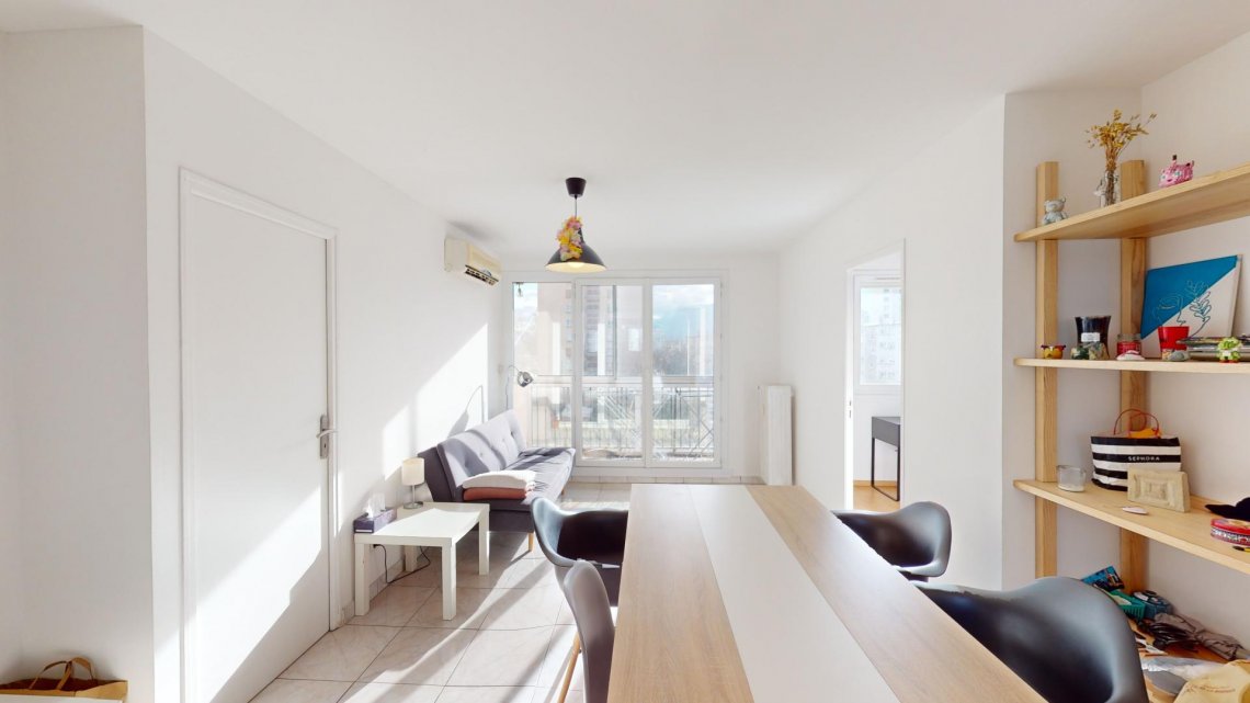 Cette colocation de quatre chambres s'ouvre sur une pièce de vie aménagée d'un canapé, deux tables basses, une bibliothèque, d'une table avec quatre chaises